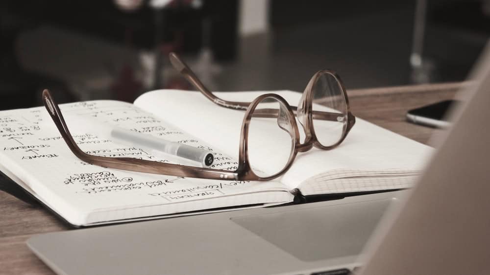 An open workbook with glasses resting on top