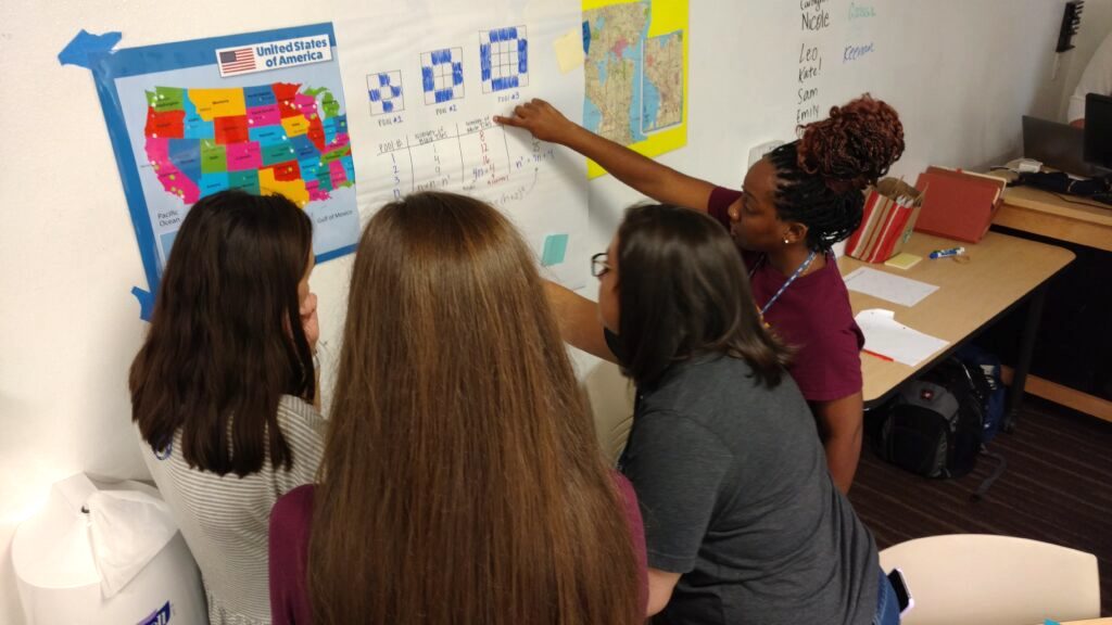 Four teachers looking at a Math poster