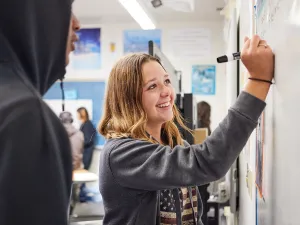 A middle school student smiling while solving a problem at the whiteboard