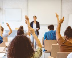 Students raising hands in classroom.